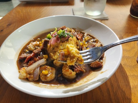 A bite of the Shrimp and Grits with roasted tomatoes, onions, sweet corn, andouille sausage and royal red shrimp at the Root and Bone in South Miami